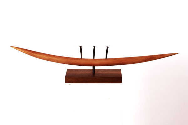 A long, gently curved wooden form with three upright dark elements, mounted on a rectangular base.