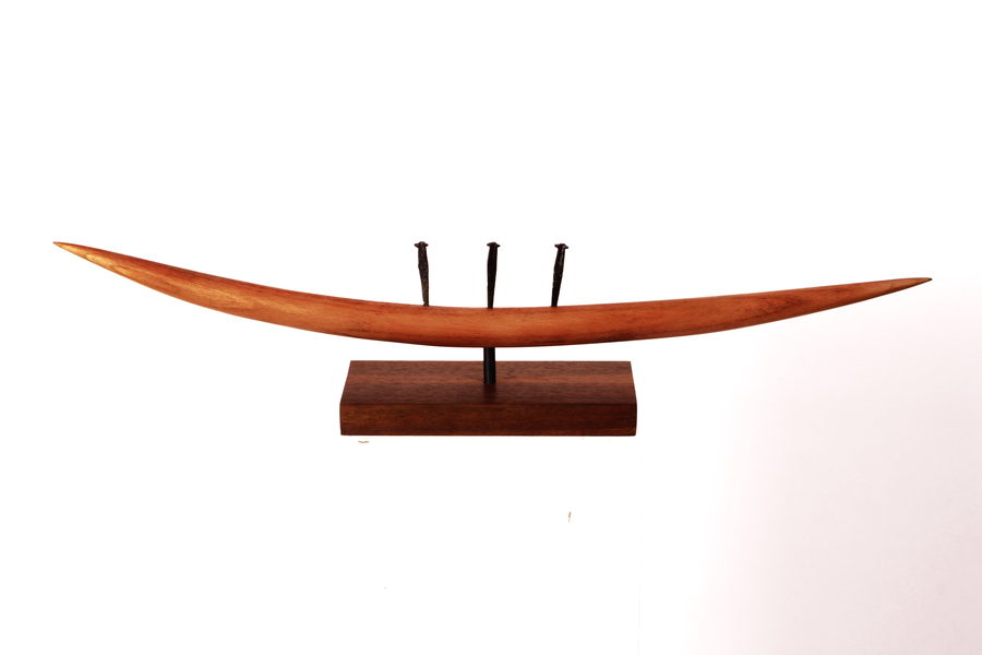 A long, gently curved wooden form with three upright dark elements, mounted on a rectangular base.