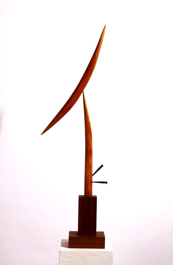 Bird in Space by Valeriu Cazacevschi. Two slender, curved wooden forms rise and cross above a rectangular wooden base, with short dark rods beside the upright.
