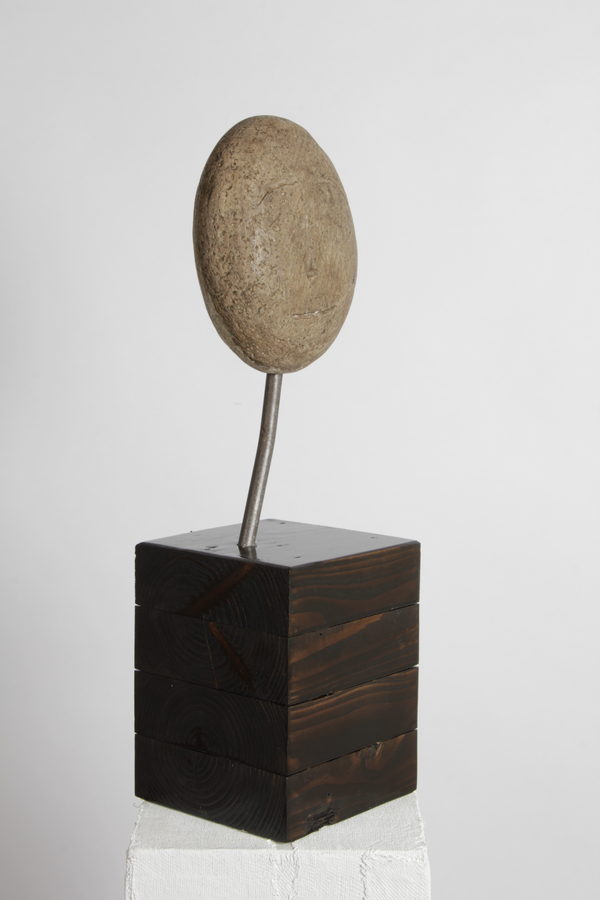Cara (2020) by Valeriu Cazacevschi. A round, stone-textured face on a curved metal stem above a dark wooden block.