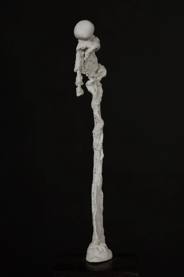 Figure of a humble Person by Valeriu Cazacevschi. A slender pale figure bows its head above a long, tapering body on a small base.