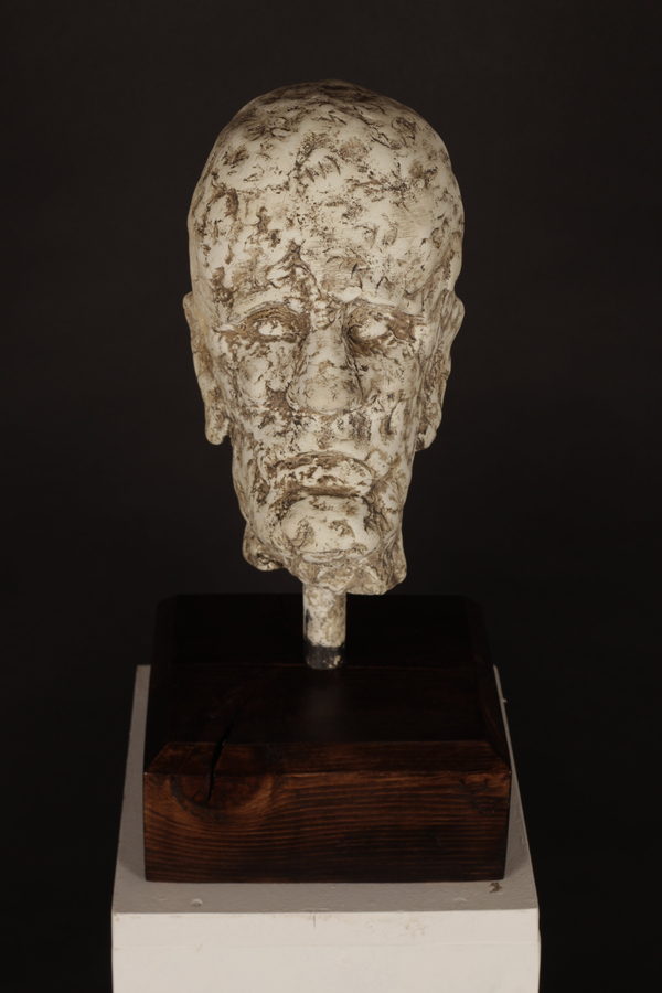 Male Head with Brown Patina by Valeriu Cazacevschi. A textured head with a brown patina is mounted on a slender dark stem above a square wooden base.