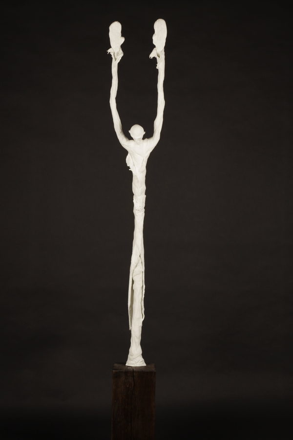 The Monk (2023) by Valeriu Cazacevschi. A tall pale figure raises both arms vertically above its head on a dark wooden support.