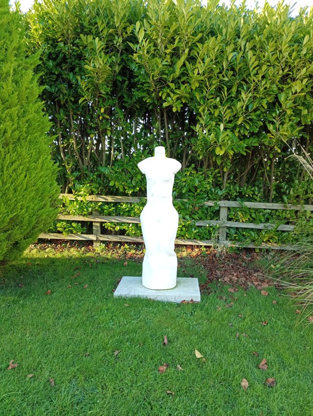 White standing torso sculpture photographed in a garden