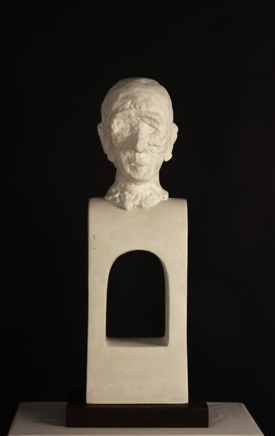 Pale sculpted head atop a rectangular base with an arched opening